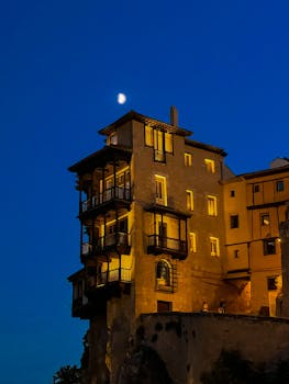Iconic Hanging Houses in Cuenca illuminated at night, under a crescent moon.