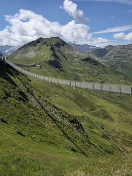 A breathtaking view of a mountainous landscape with a long suspension bridge stretching across lush green hills.