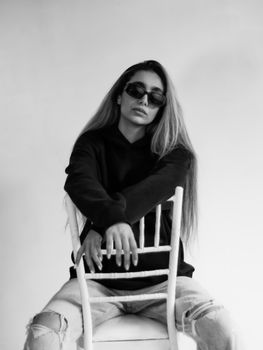 Black and white portrait of a stylish young woman posing indoors wearing sunglasses.