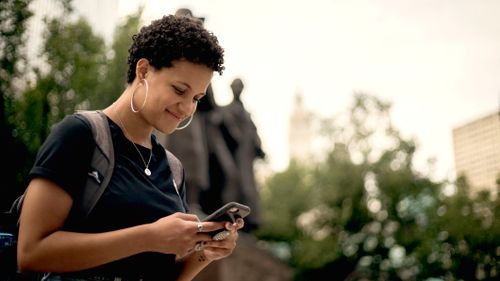 Free Smiling woman with curly hair texting on her phone in Chicago park. Stock Photo