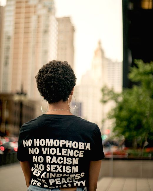 Person standing outdoors in Chicago, wearing a T-shirt advocating kindness and peace. Urban cityscape background.