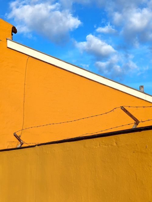 Free Bright yellow wall against a vivid blue sky with clouds, showcasing minimalistic architectural geometry. Stock Photo