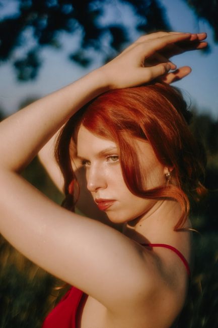 Portrait of a young woman with red hair posing gracefully outdoors in a red dress.