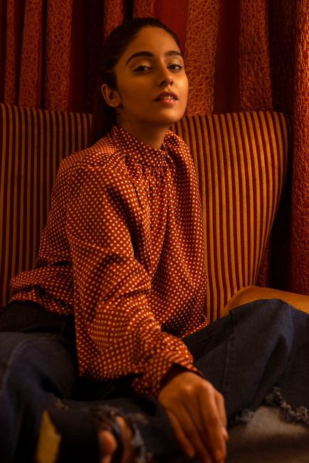 Elegant woman in a polka-dot blouse posing indoors, showcasing style and grace.