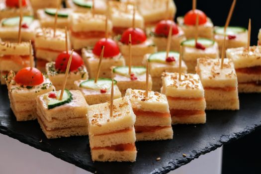 Delicious mini sandwiches adorned with cherry tomatoes and cucumber slices on slate.