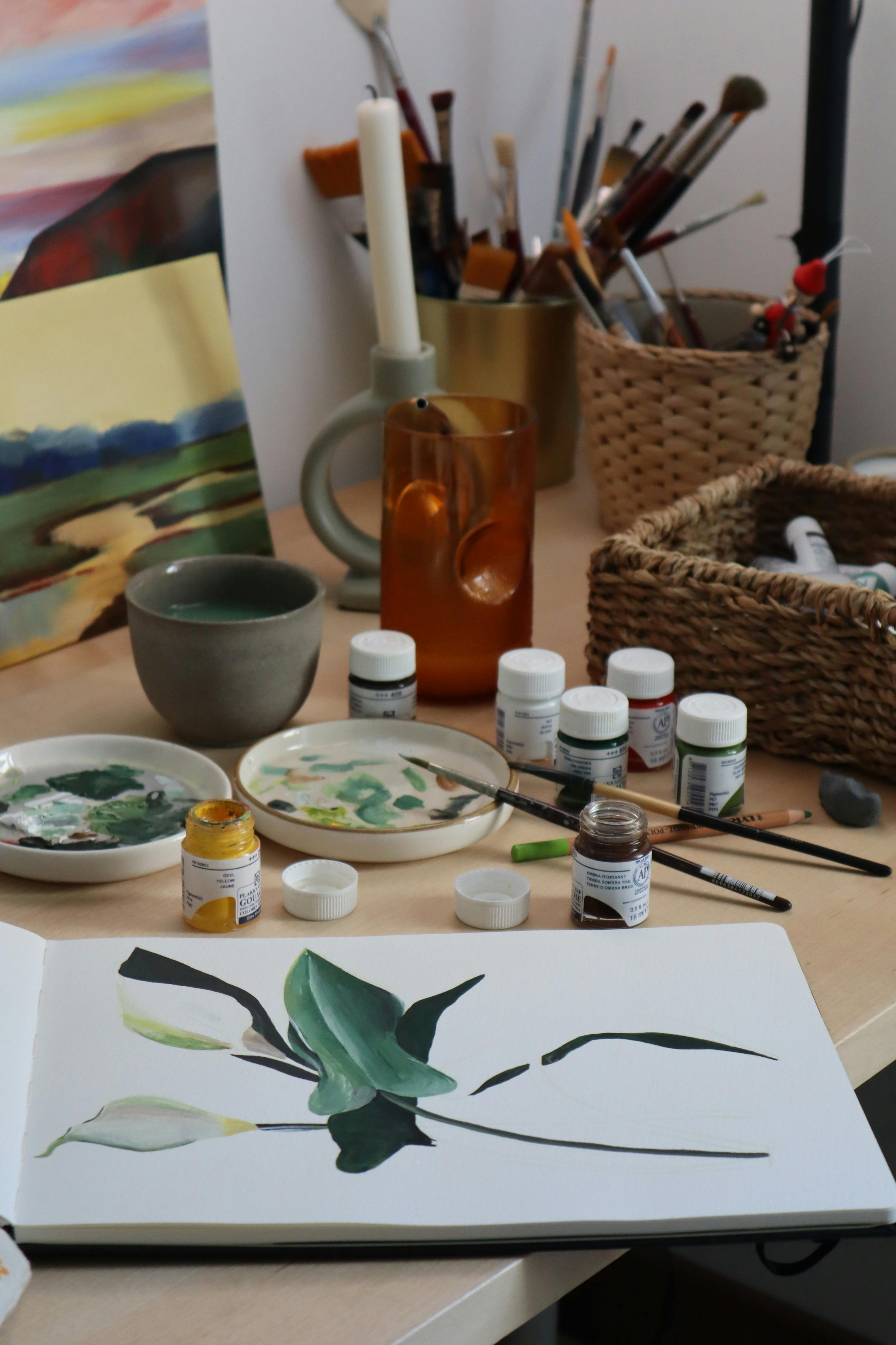 Artistic setup with painting supplies and canvas featuring a botanical illustration.