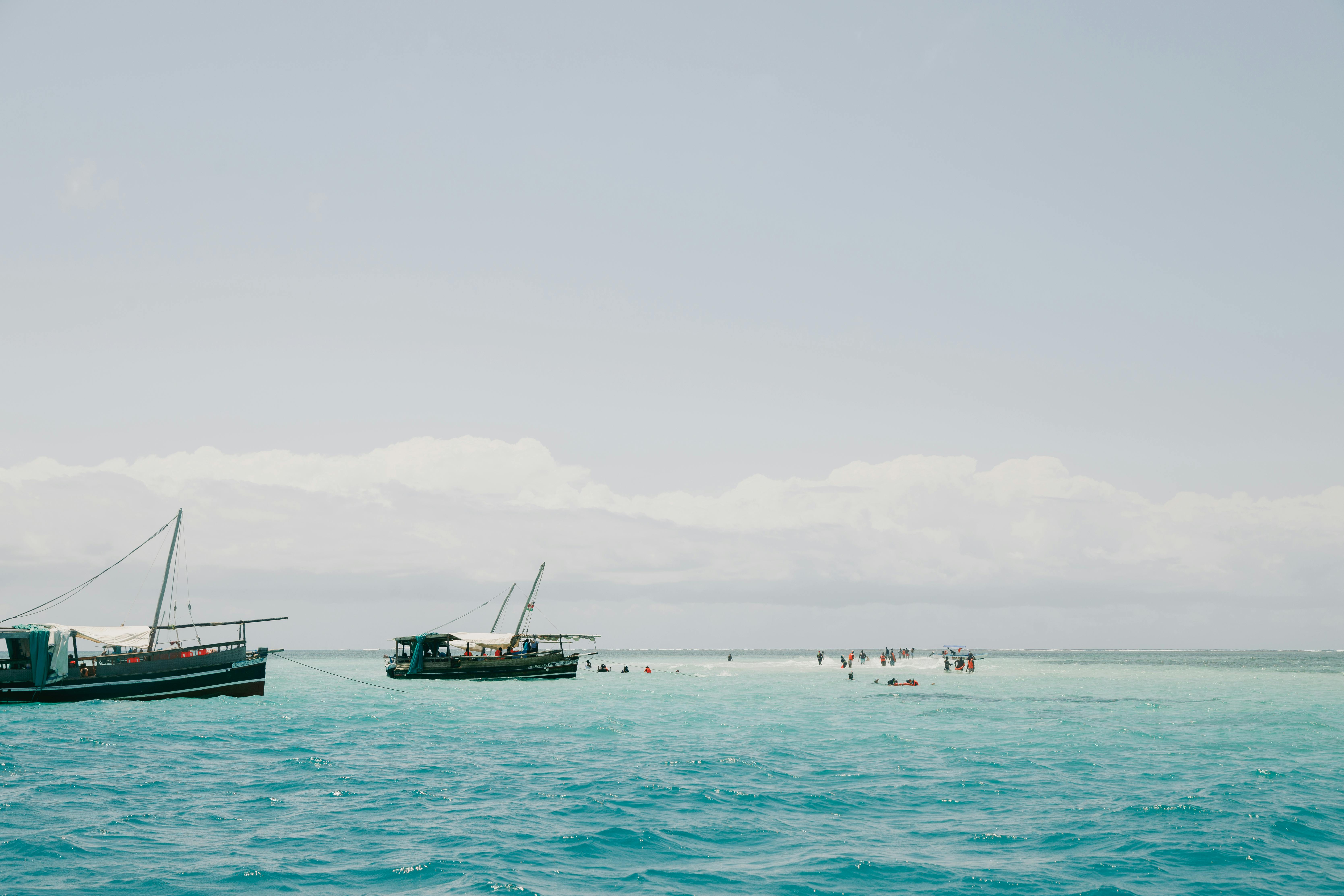 Traditional boats float in crystal-clear waters near Mombasa, Kenya, under a bright summer sky.