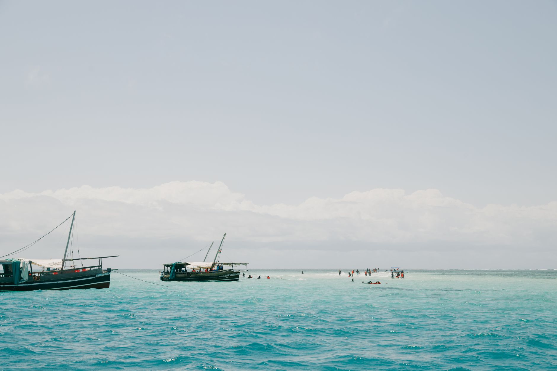 Traditional boats float in crystal-clear waters near Mombasa, Kenya, under a bright summer sky.