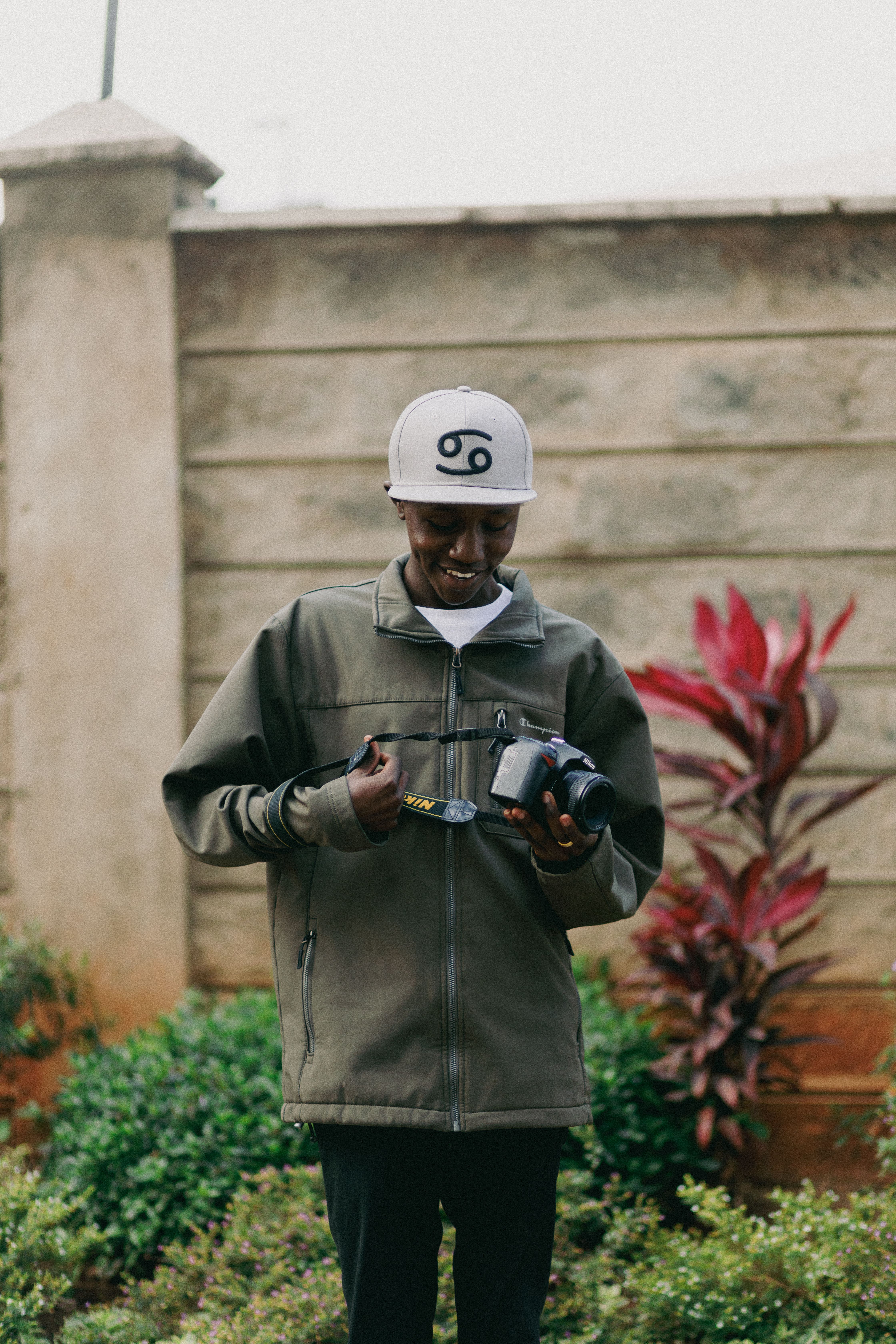 A young man enjoys photography outdoors in Mombasa, Kenya, holding a camera and wearing casual attire.