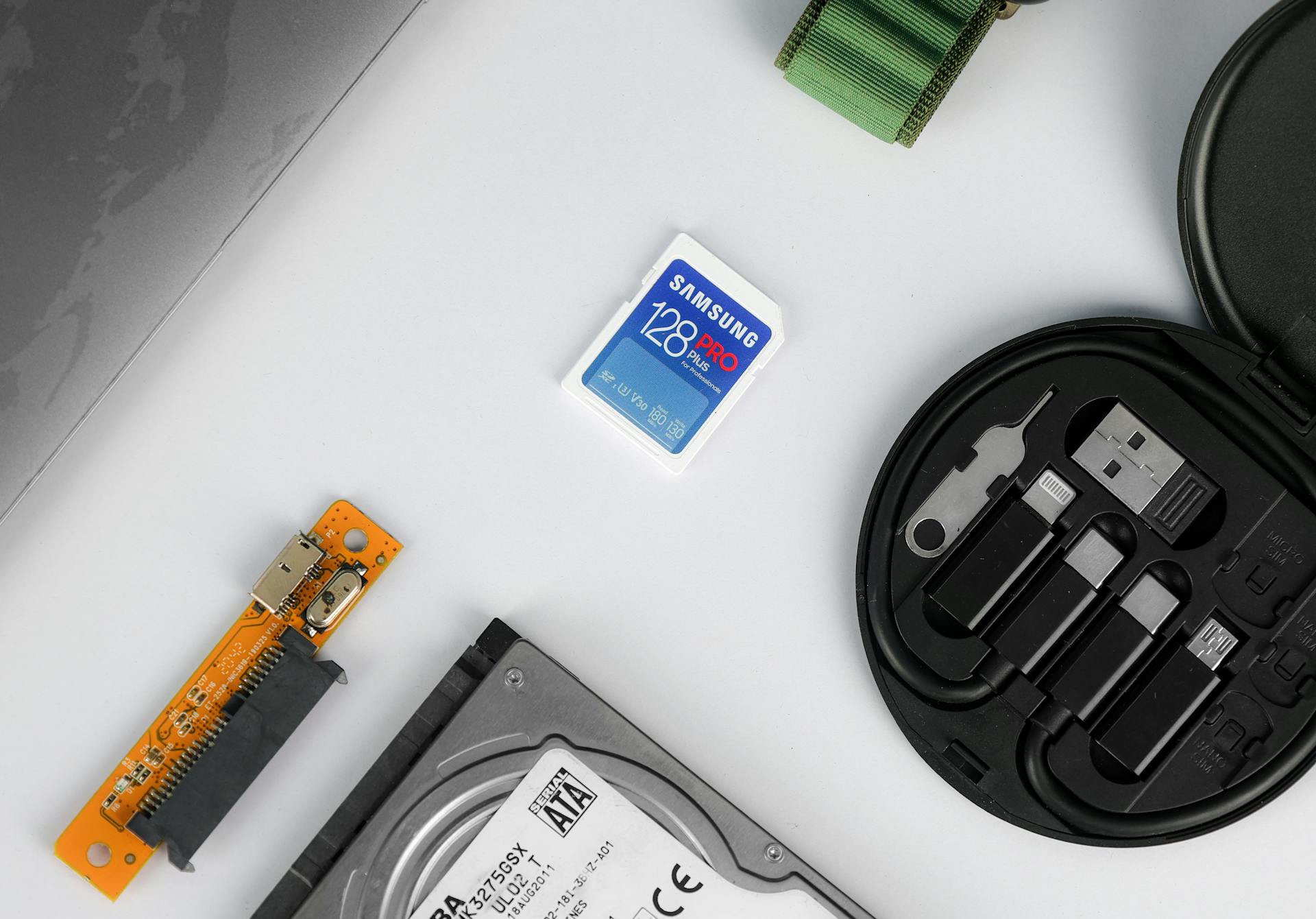 Flat lay of various technical components including a memory card and hard drive on a white background.