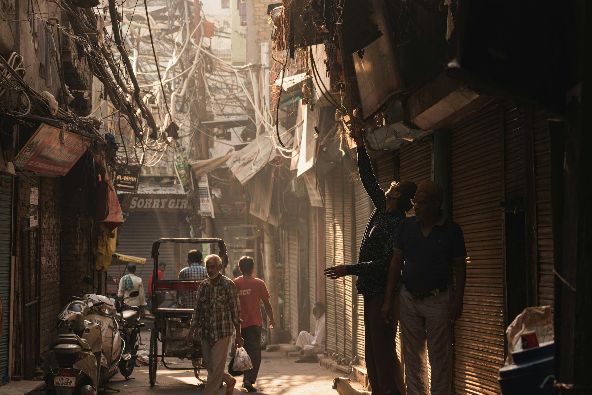 A busy urban alleyway with people and tangled electrical wires in soft light.