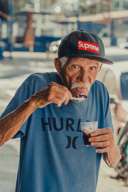Senior man savoring a sweet treat outdoors, wearing a trendy cap and casual outfit.