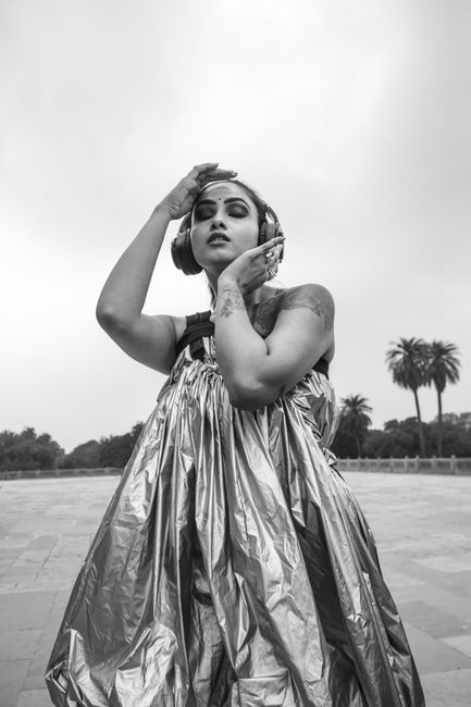 Monochrome photo of a stylish woman posing elegantly in an outdoor location with dramatic expression.