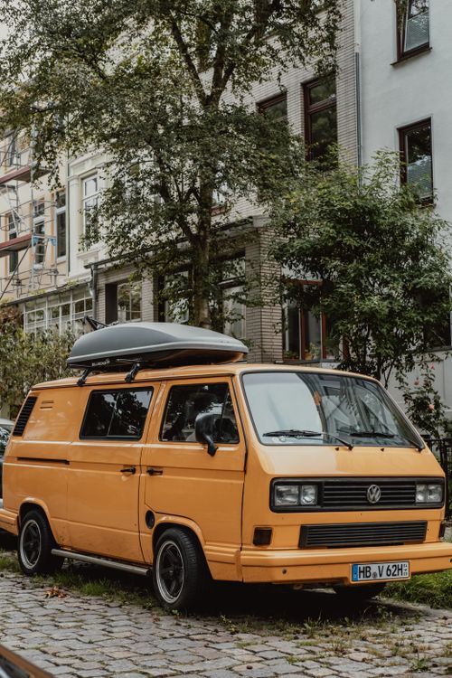 Free Classic yellow Volkswagen van parked on a cobblestone street in Bremen, Germany with urban backdrop. Stock Photo