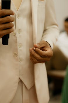 Groom in stylish suit holding wedding ring during indoor ceremony.