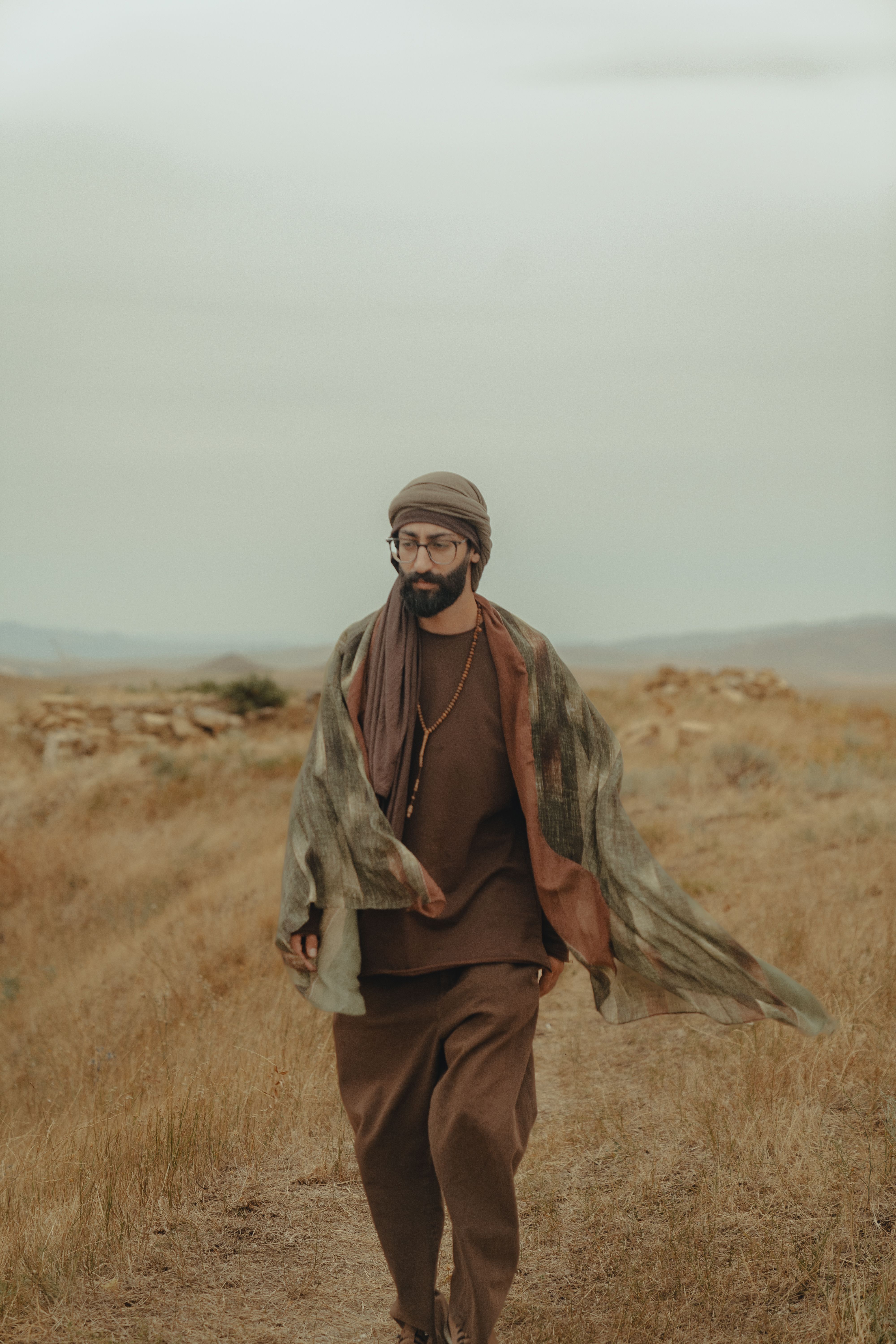 A man wearing a turban is strolling through the rustic countryside on a serene day.