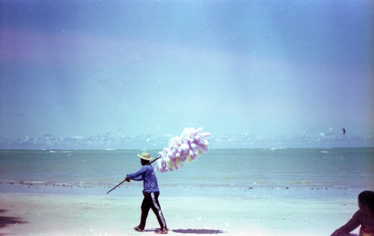 A man carrying colorful cotton candy on a peaceful seashore during a bright day.