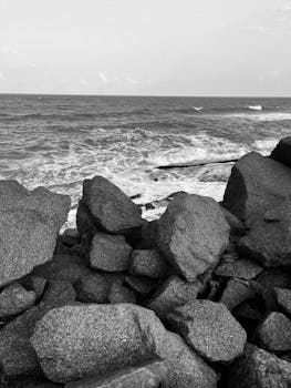 Serene black and white view of ocean waves crashing against rocky shore.