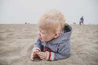 一个顽皮的金发幼儿在美国加利福尼亚州的狄龙海滩开心地玩沙子