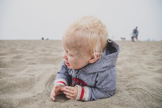 一个顽皮的金发幼儿在美国加利福尼亚州的狄龙海滩开心地玩沙子