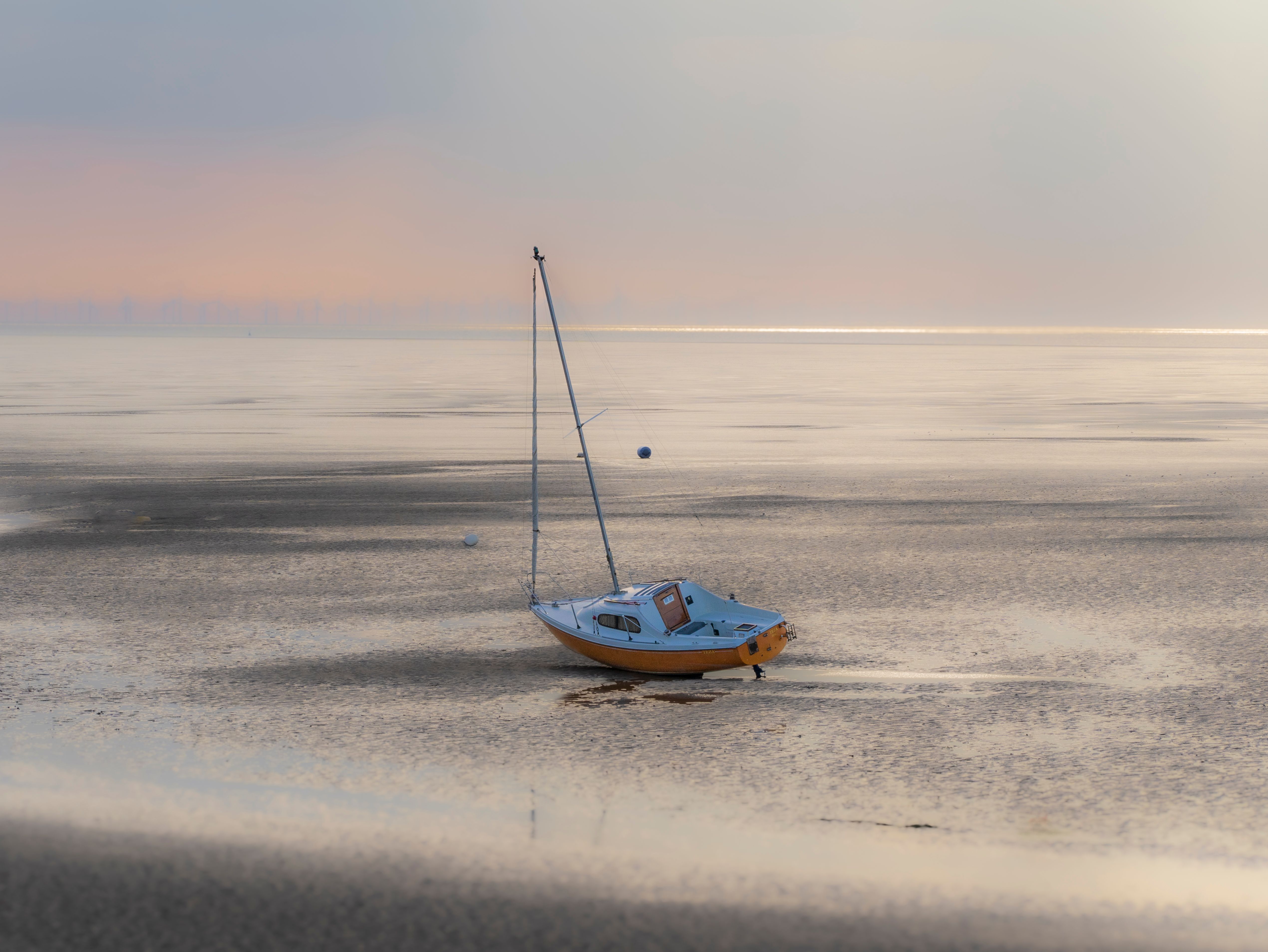 A tranquil scene of a boat resting on the sandy shore at West Kirby during a calm sunset, perfect for travel inspiration.