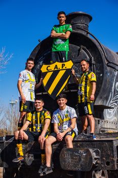 Five male soccer players posing on an old train under clear blue skies.