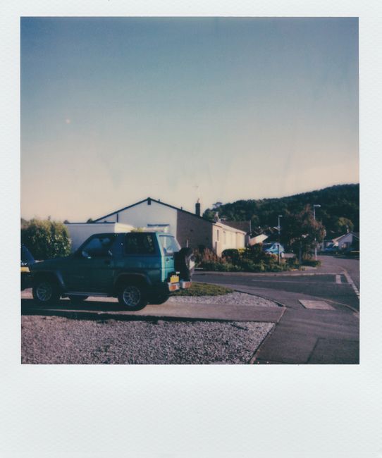 A nostalgic Polaroid image capturing a parked car in a quiet suburban neighborhood on a sunny day.