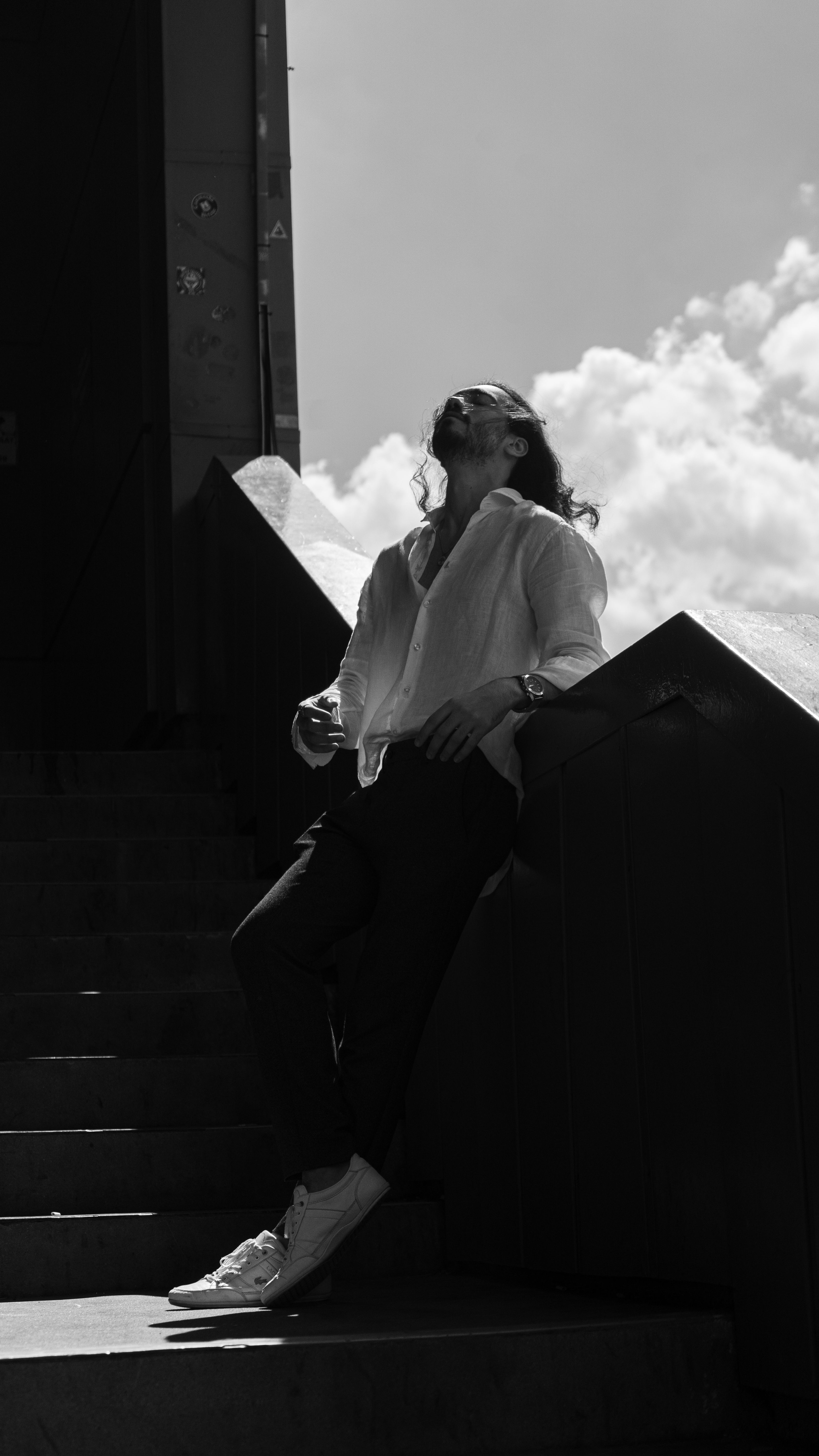 A man leaning against stairs outdoors, reflecting under a bright sky.