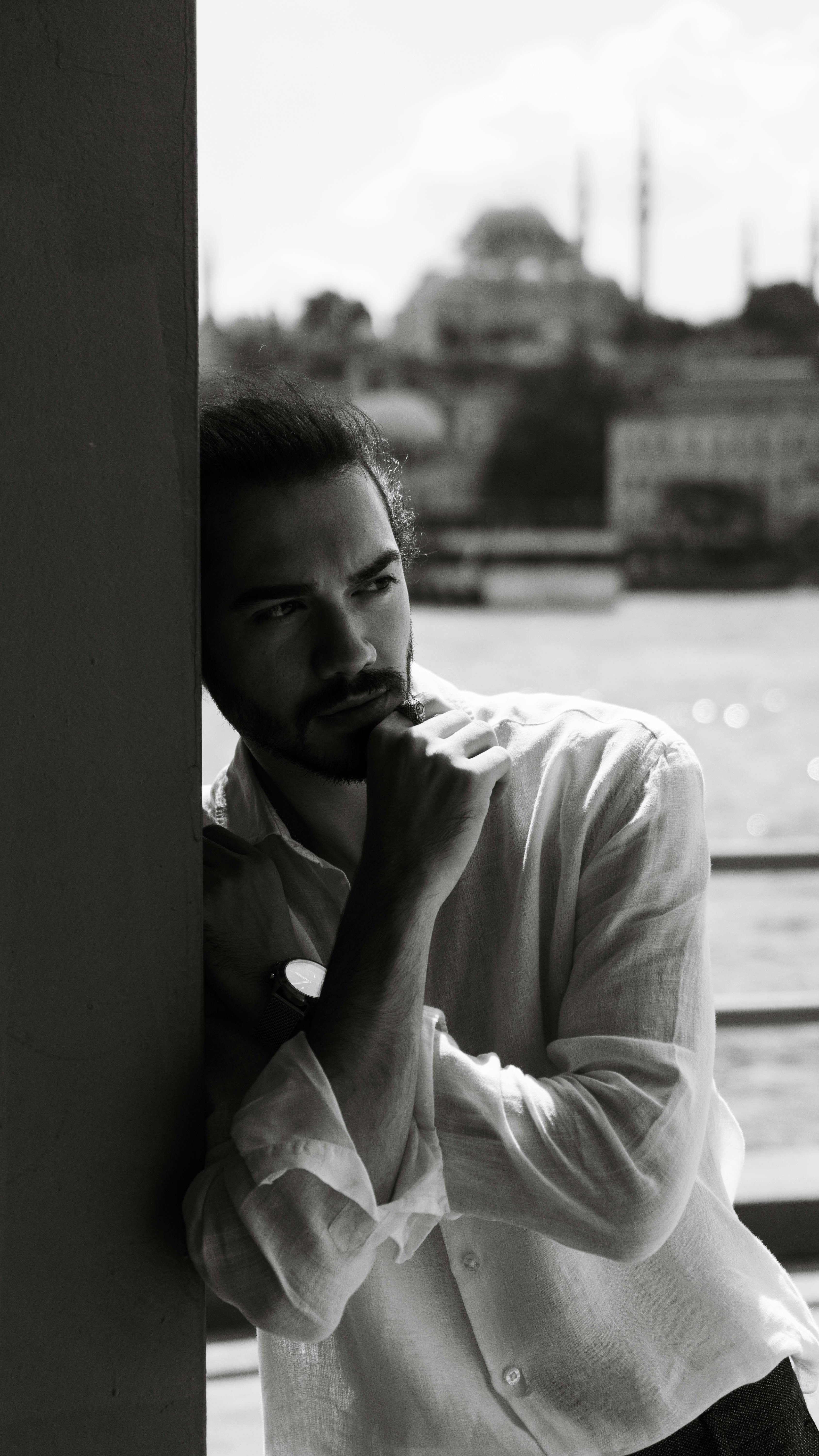 Thoughtful man in monochrome leaning on pillar with cityscape background.