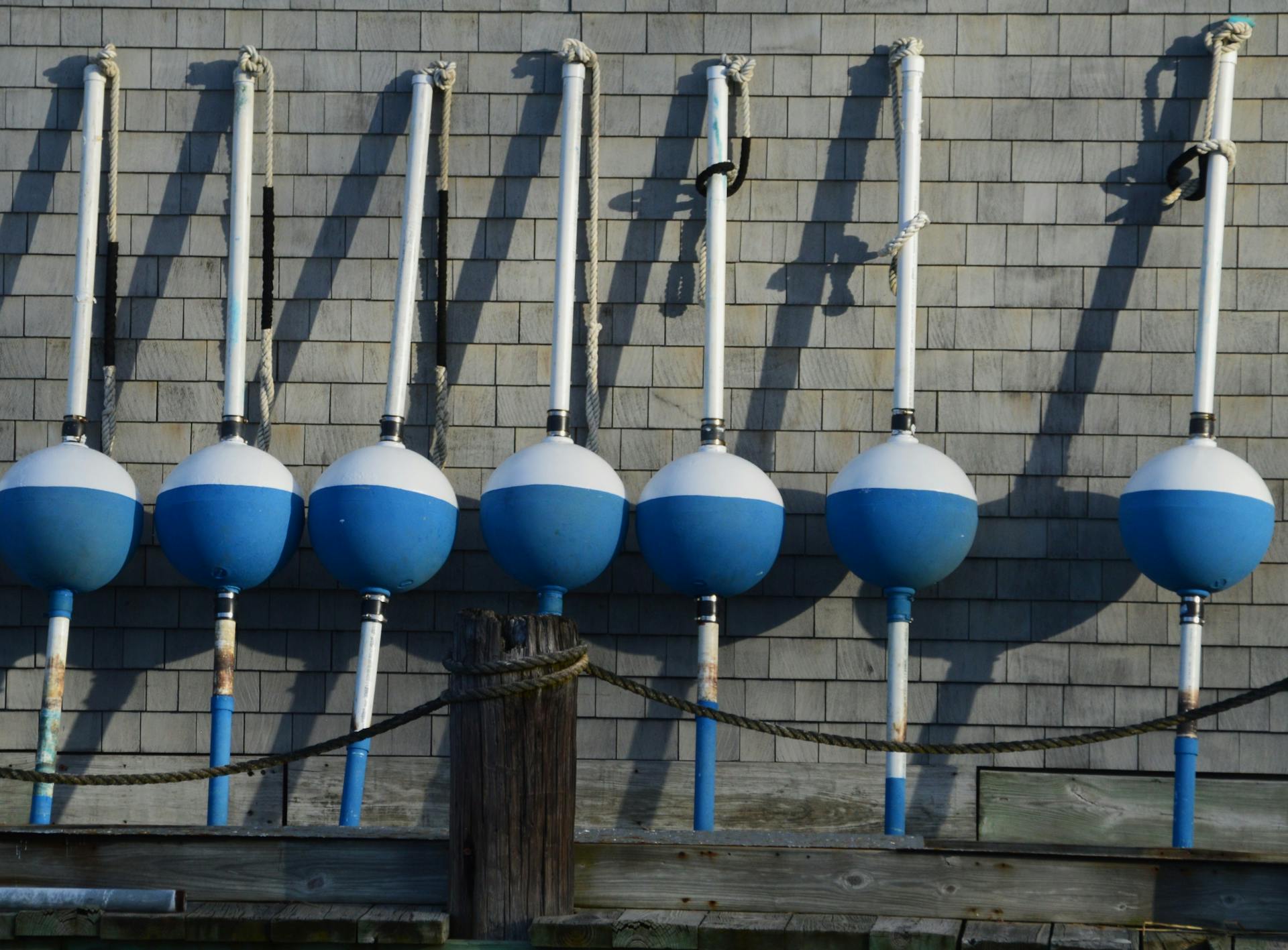 Blue and white nautical buoys aligned against a shingled wall in Northport, NY.
