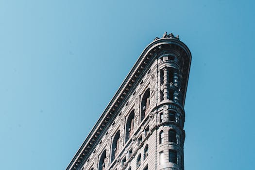 Iconic Flatiron Building in New York City under a bright blue sky, captured from a low angle.