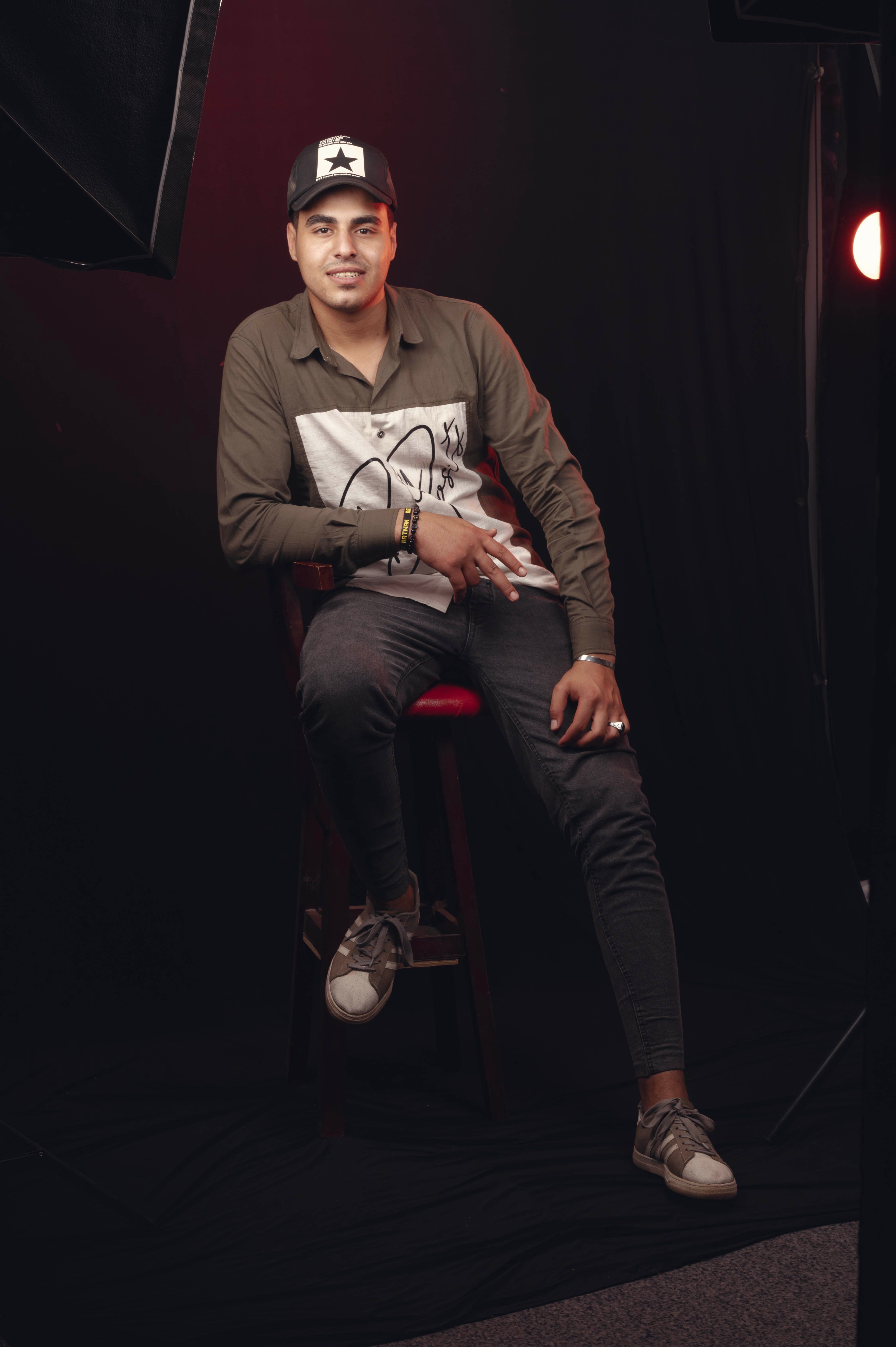 Studio portrait of a casually dressed man seated on a stool, looking at the camera.