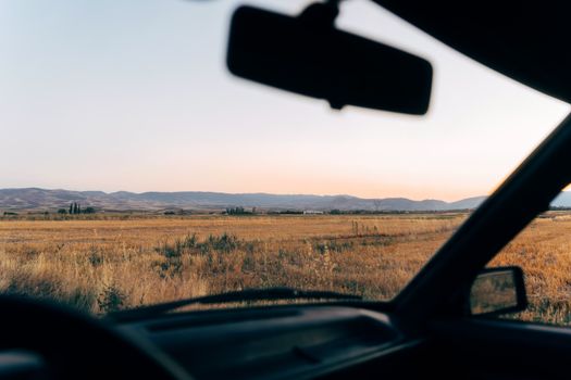 Experience a serene sunset drive through vast open fields seen from a car interior.