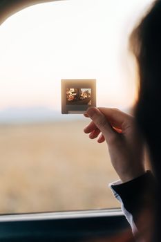 A hand holds slide film against a blurred sunset view, capturing a nostalgic moment.