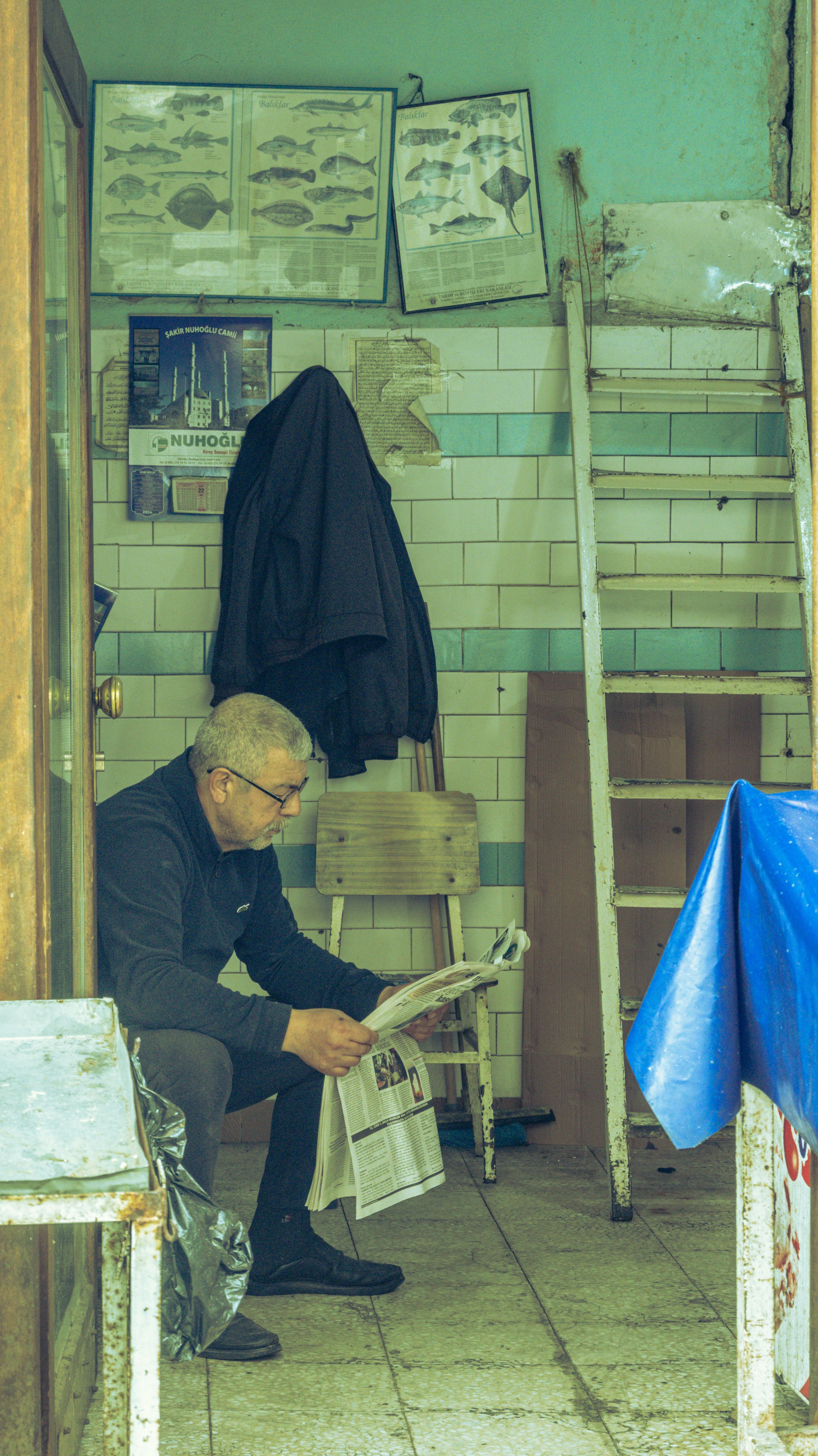 Man seated indoors reading a newspaper in a rustic room with industrial decor.