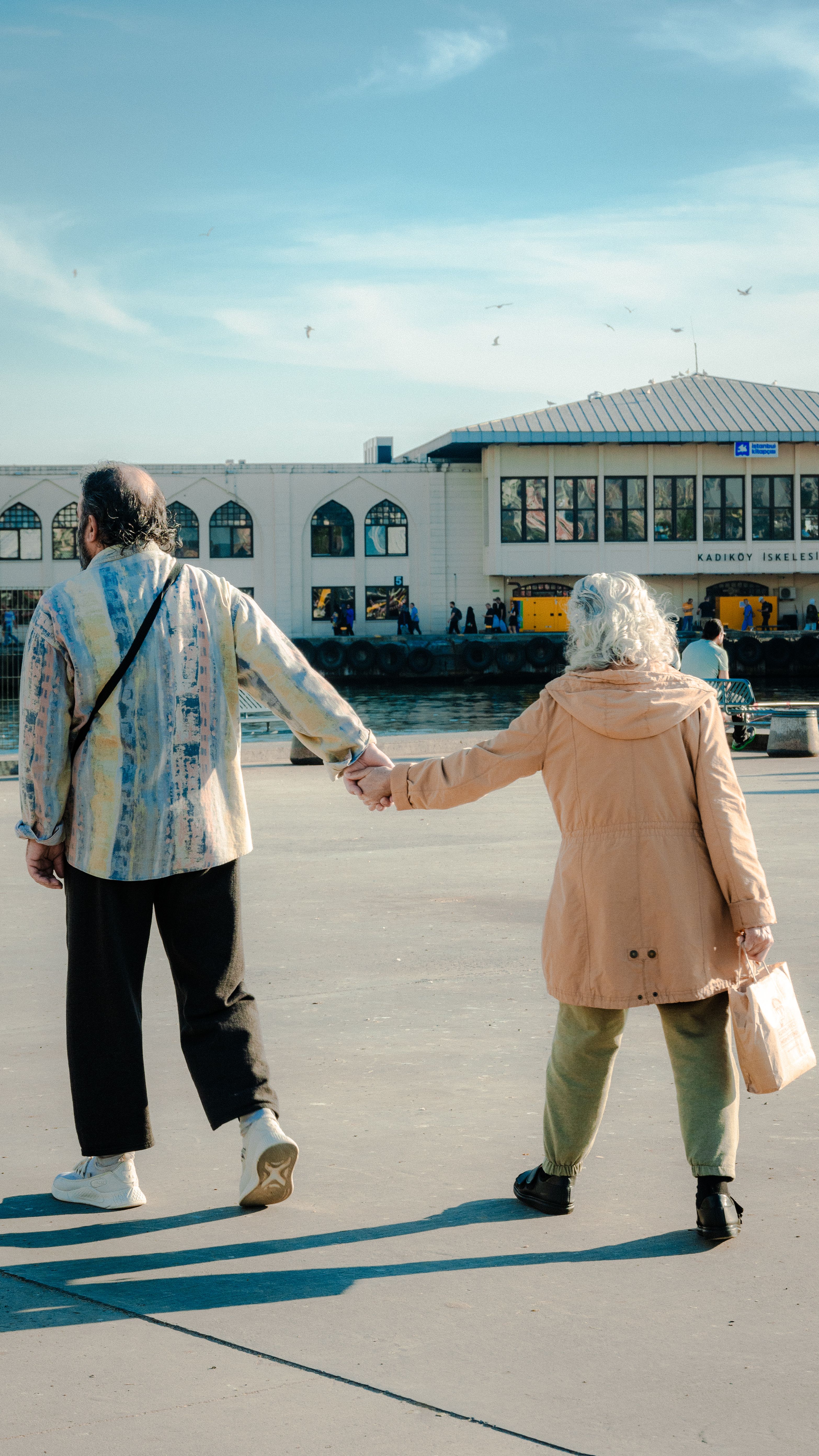 An older couple holding hands walking down a sidewalk · Free Stock Photo