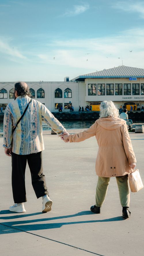 Free Elderly couple holding hands during a stroll by a city pier, symbolizing companionship and outdoor leisure. Stock Photo