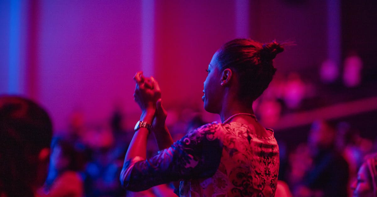 A woman claps at a concert, surrounded by a crowd in vivid purple and red lighting.
