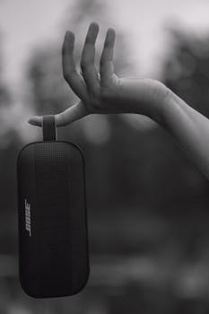 A graceful hand holding a portable speaker in a monochrome outdoor setting, conveying modern technology.