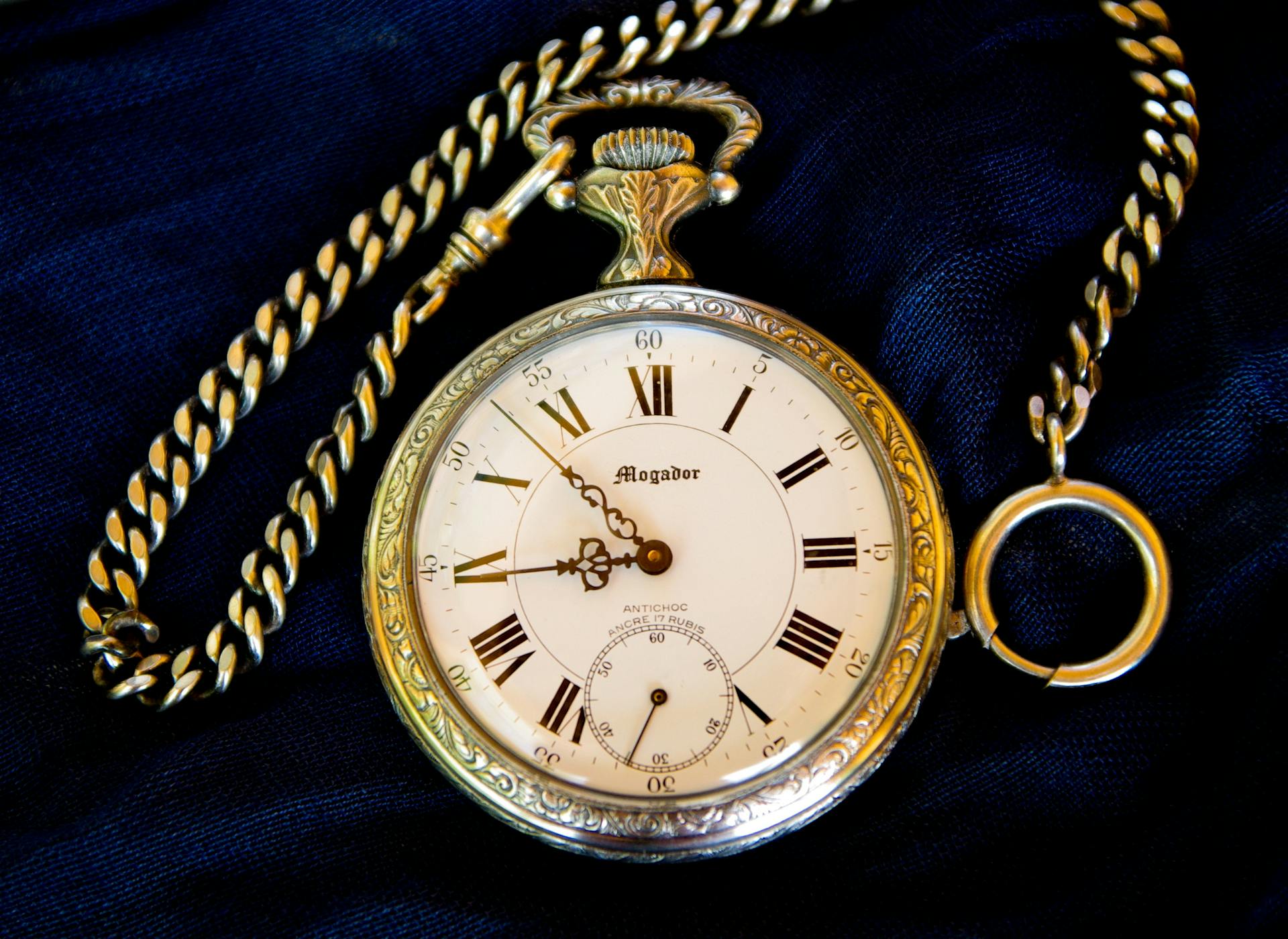 Classic vintage pocket watch with intricate design and gold chain on a dark fabric.