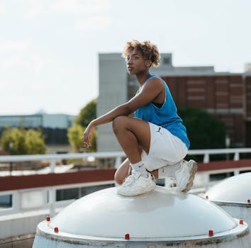Dynamic urban portrait of a woman in sportswear crouching on a rooftop, embodying athletic style and city vibes.