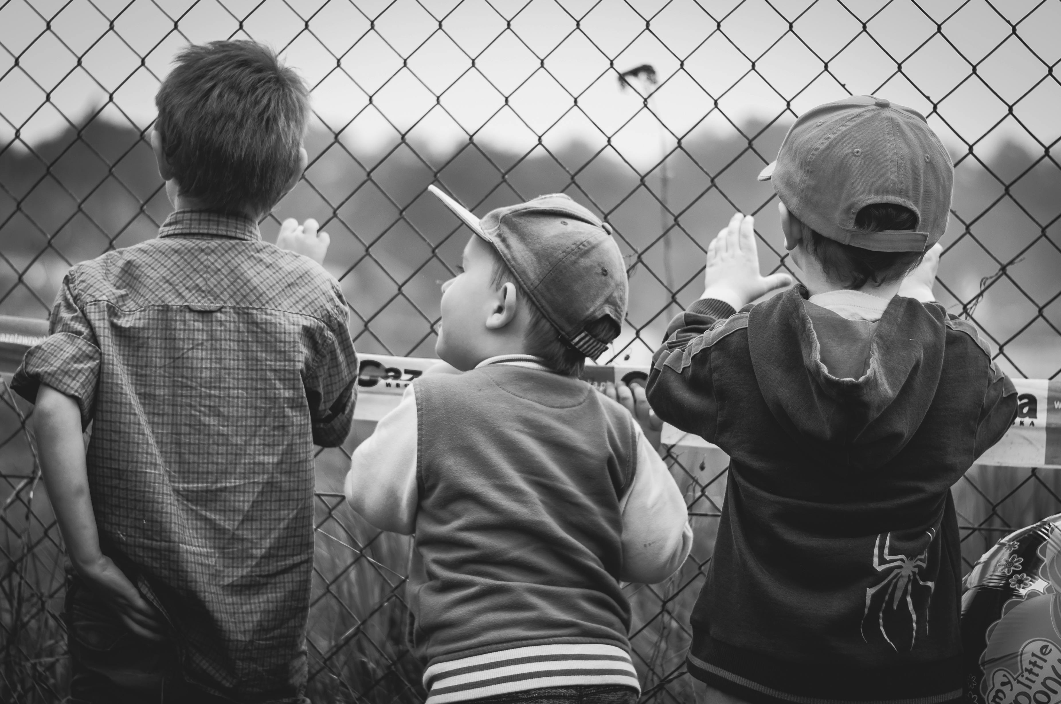 Three children facing towards fence. | Photo: Pexels