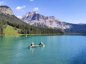 两个人在翡翠湖的原始水域划独木舟，欣赏着雄伟的山景