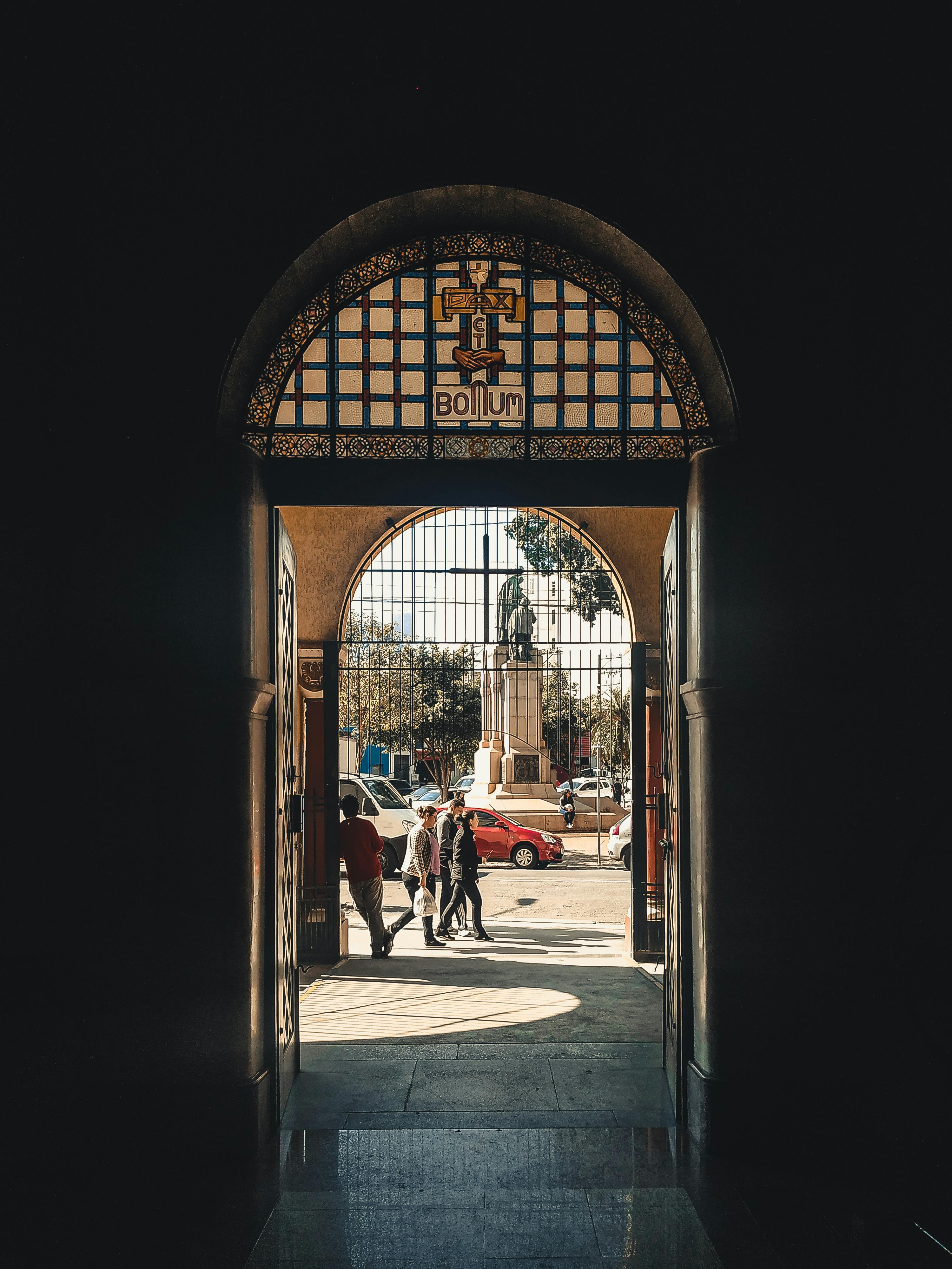 城市场景通过一个拱门框架展现，雕像和人们在户外行走