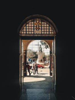 城市场景通过一个拱门框架展现，雕像和人们在户外行走