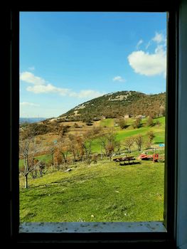 A picturesque landscape of fields and hills seen through an open window, capturing nature's beauty.