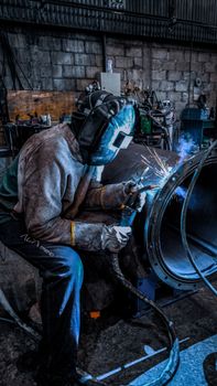 A worker welding inside a factory in Brazil, wearing safety gear and helmet.