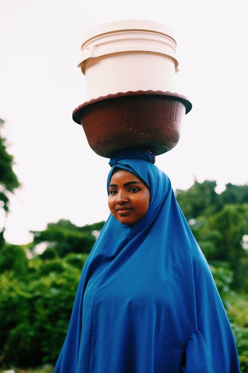 Free Portrait of a woman balancing containers on her head in a vibrant outdoor setting. Stock Photo