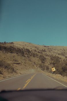 A serene highway cutting through arid hills under a vast, clear sky on a sunny day.