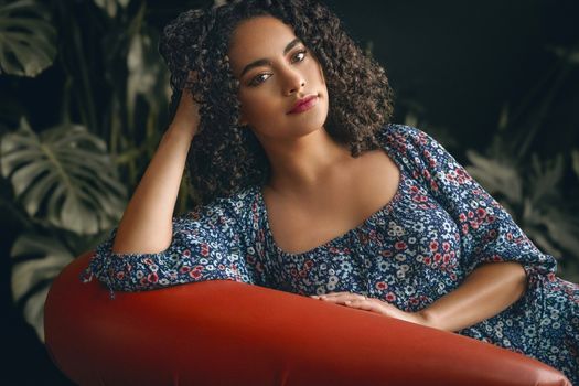 Portrait of a woman in a floral dress relaxing indoors on a red couch.